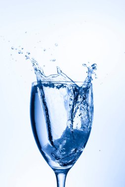 Açık mavi arkaplanda bardağa su sıçrıyor.