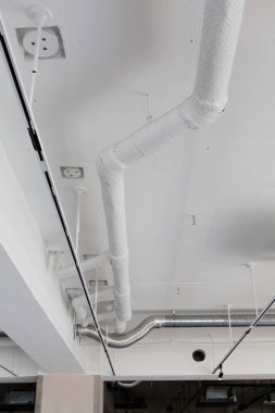 Beyaz tavanda açıkta duran borular elektrik prizleri ve metal borular var.