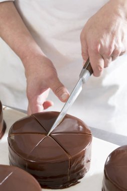 Bir pastanede çikolatalı pasta dilimlenirken bir pasta şefi müşterilere tatlı servis etmeye hazırlanıyor.