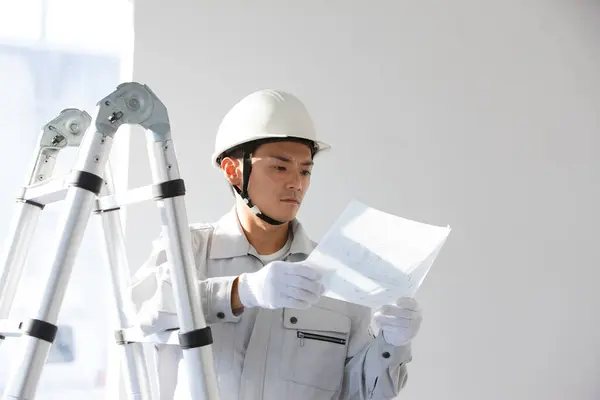 portrait of handsome young Japanese builder in uniform at construction site