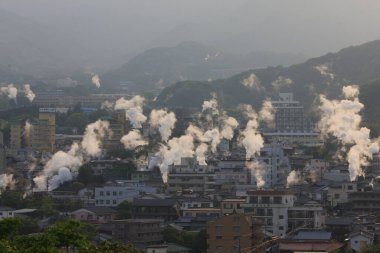 Sisli bir sabahta şehir binalarının üzerinde yükselen bacalar.