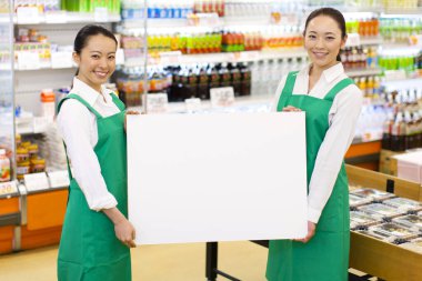 Asyalı kadın personel süpermarketin önünde boş tabela tutuyor.