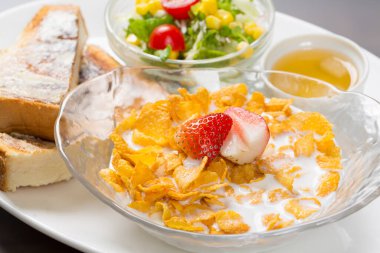 Mısır gevreği, taze meyve, salata ve tostun beyaz tabakta servis edildiği lezzetli bir kahvaltı.