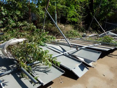 Kırık dalların arasında duran hasarlı metal çit panelleri.