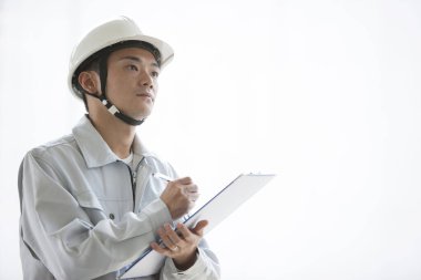 Üniformalı yakışıklı Japon inşaatçının portresi. İnşaat alanını pano ile inceliyor.