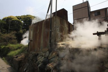 Paslı metal yapı, çimenli yamaçların yanında kalın buhar yayıyor.