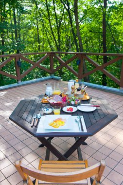 Yeşil ağaçlarla çevrili açık hava kahvaltı masası.