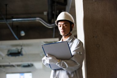 Üniformalı yakışıklı Japon inşaatçının portresi. İnşaat alanını pano ile inceliyor.