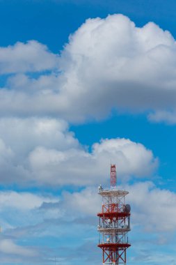 Kırmızı beyaz iletişim kulesi parlak mavi gökyüzü bulutlarının karşısında duruyor.