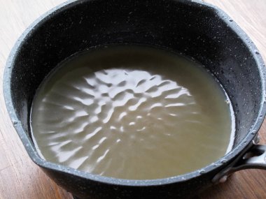 Siyah tencere ahşap yüzeyde kaynayan bulutlu bir sıvı tutuyor.