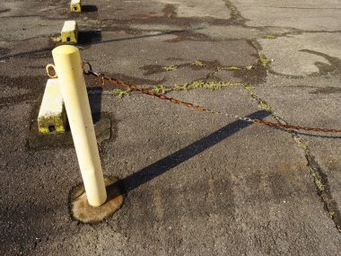Yellow pole casting shadow on cracked pavement with weeds