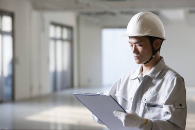 Üniformalı yakışıklı Japon inşaatçının portresi. İnşaat alanını pano ile inceliyor.