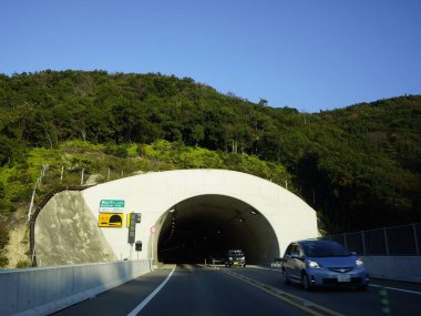 Arabalar berrak mavi gökyüzünün altındaki dağ tüneline doğru gidiyor.