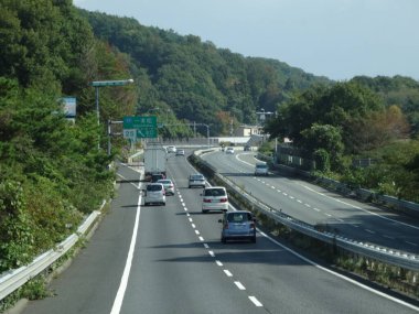 Çevrede yeşil ağaçlarla çevrili otoban boyunca giden arabalar