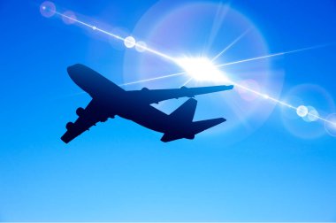 Uçak gökyüzünde uçuyor, arkasında güneş parlıyor.