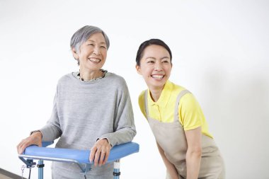 Bayan Bakıcı engelli yaşlı Asyalı kadının Walker 'la durmasına yardım ediyor.