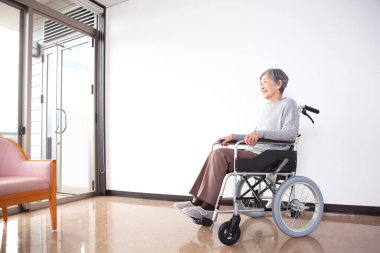 Hastanede tekerlekli sandalyede oturan gülümseyen yaşlı Asyalı kadın. 