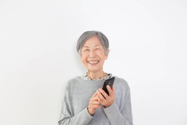 Üst düzey Asyalı kadın beyaz arka planda akıllı telefon kullanıyor. 