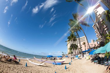 İnsanlar tropik deniz kıyısındaki palmiye ağaçlarıyla kumsalda dinleniyorlar.                         