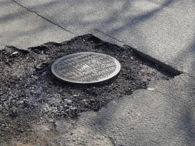 Açığa çıkan metal rögar kapağını çevreleyen asfalt hasar görmüş.
