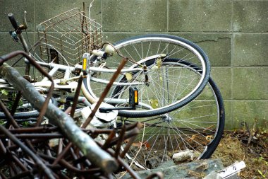 Paslı bisikletler beton duvarlara yaslanıyor. Metal enkaz yığınlarının yanında.