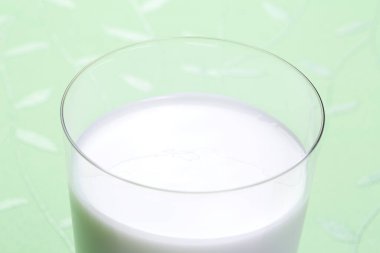 Açık yeşil arka planda bir bardak taze süt