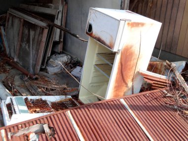 Paslı buzdolabı enkaz ve atıklarla çevrili.