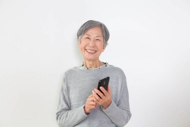 Üst düzey Asyalı kadın beyaz arka planda akıllı telefon kullanıyor. 