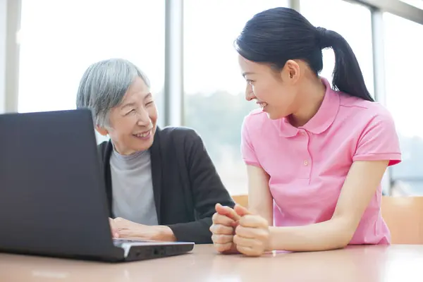 若いアジアの女性は家庭でラップトップを使用するために高齢女性を教えています — ストック写真