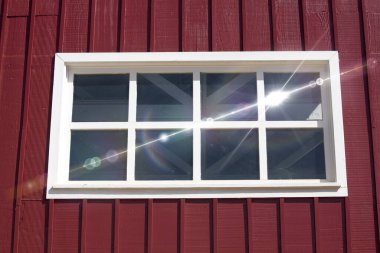 Kırmızı ahşap duvardaki beyaz çerçeveli pencereden yansıyan güneş ışığı