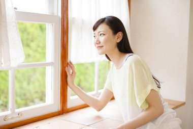 Genç Asyalı kadın oturma odasının penceresinden bakıyor.