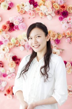 Arka planda çiçeklerle gülümseyen genç Asyalı kadın. 