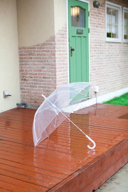 Şeffaf şemsiye kapının yanındaki ıslak ahşap güvertede duruyor.