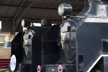 Klasik siyah buhar lokomotifleri ahşap çatı altında duruyor.