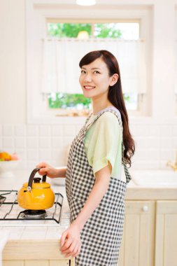 Mutfakta sarı çaydanlığı olan Asyalı kadın.