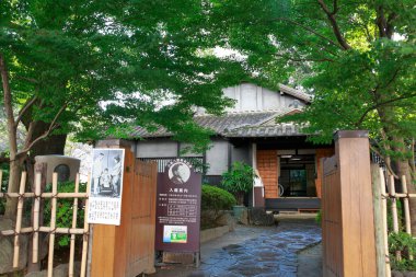 Geleneksel Japon evi yemyeşil ağaçlar ve ahşap kapılarla çevrili.