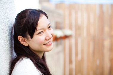 Asyalı genç kadın gülümsüyor ve kameraya bakıyor.