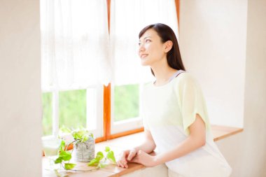 Genç Asyalı kadın oturma odasının penceresinden bakıyor.