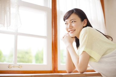 Genç Asyalı kadın oturma odasının penceresinden bakıyor.