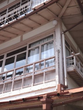 Güneşli, ahşap balkon. Cam pencereler ve beyaz perdeler var.