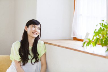 Genç Asyalı kadın oturma odasının penceresinden bakıyor.