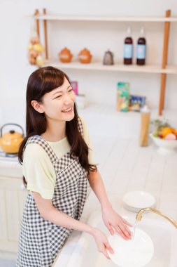 Asyalı kadın beyaz tabağı sabunla yıkıyor.