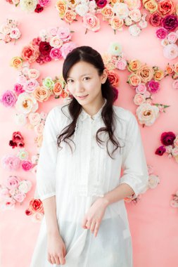 Beyaz elbiseli kadın çiçeklerin önünde duruyor.