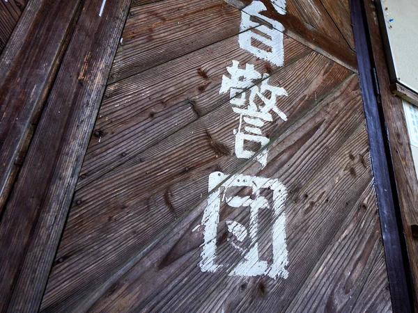 Soluk beyaz karakterler ve dokulardan oluşan eskimiş ahşap bir kapı.