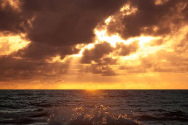 Bulutlar ve güneş ışınlarıyla denizin üzerinde güzel bir gün batımı