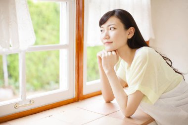 Genç Asyalı kadın oturma odasının penceresinden bakıyor.