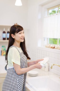 Asyalı kadın beyaz tabağı sabunla yıkıyor.