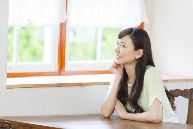 Genç Asyalı kadın mutfakta pencere kenarında oturuyor.