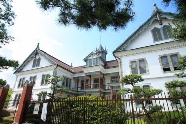 Yeşil ağaçlarla çevrili dik çayırlara sahip tarihi beyaz bina.