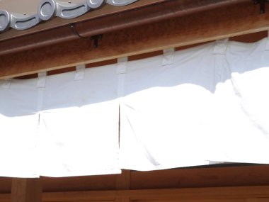 Beyaz kumaş güneş ışığında ahşap yapının altında asılı.